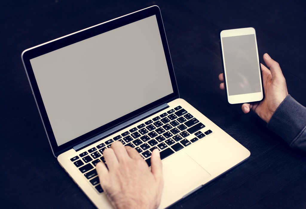 Closeup of hand holding mobile phone with computer laptop background